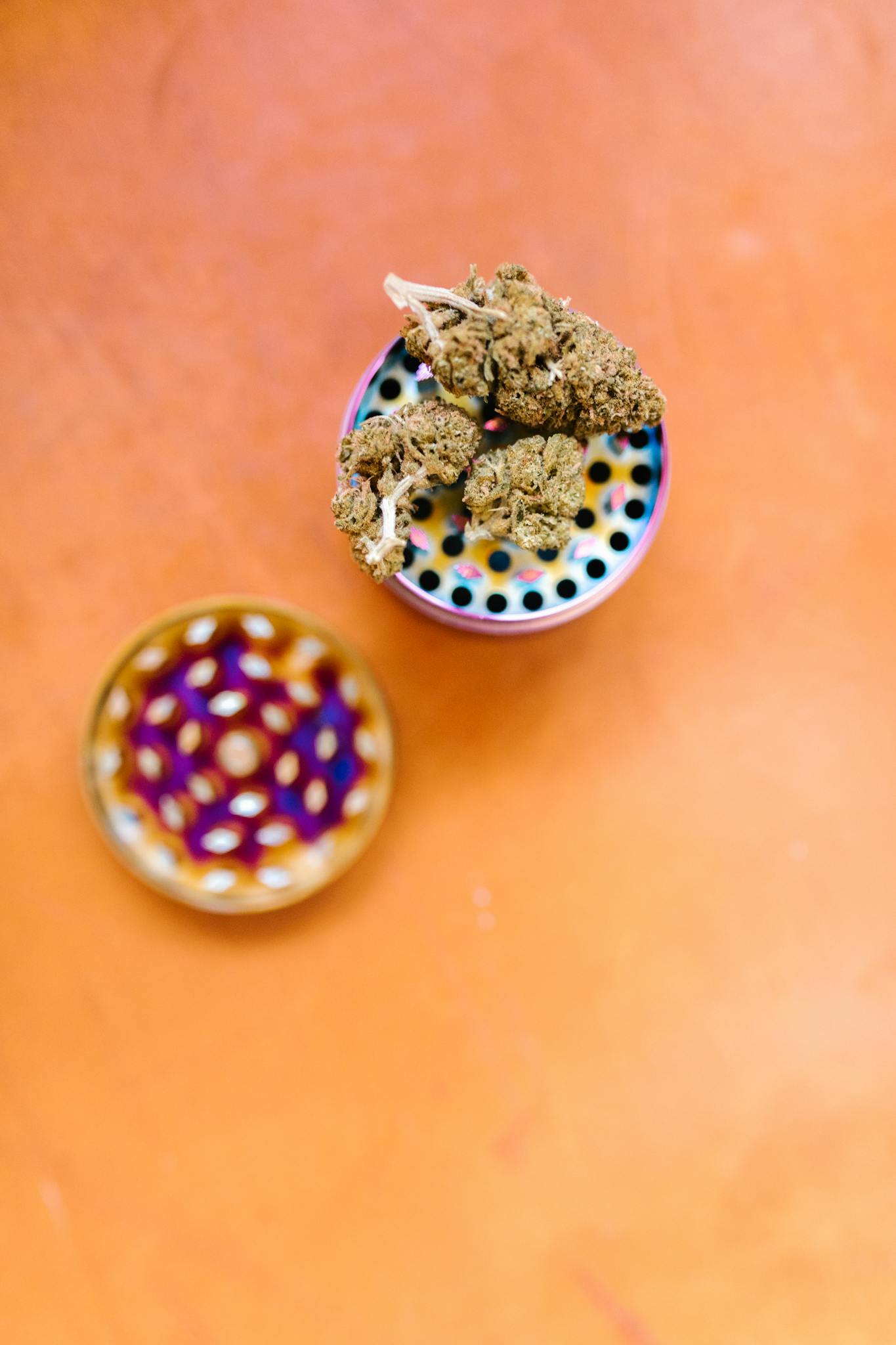 Top view of marijuana buds on a colorful grinder against an orange surface, emphasizing cannabis culture.